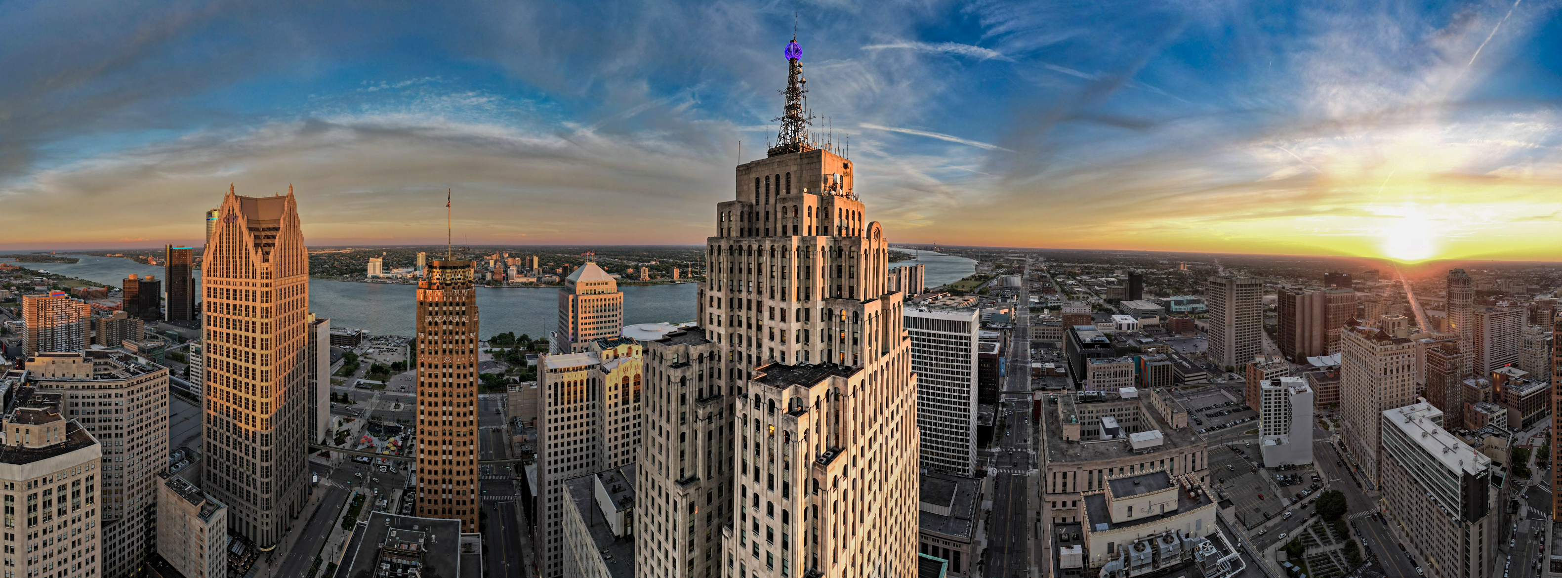 Aerial view of a cityscape with skyscrapers at sunset, vibrant sky, and a river in the background.